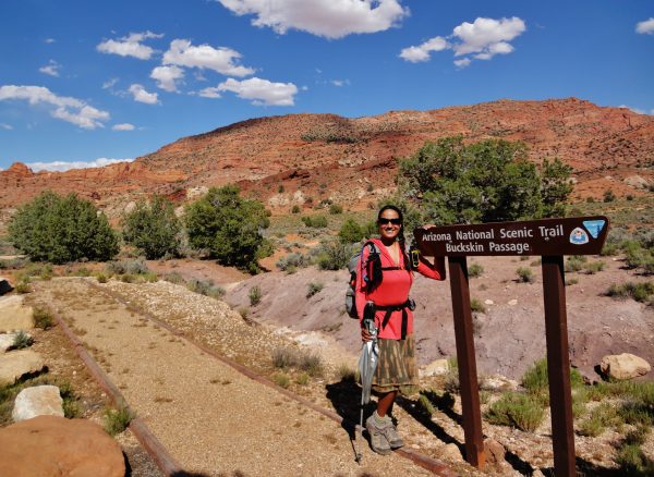 Woman with backpack stands next to sign that says Arizona National Scenic Trail, Buckskin Passage